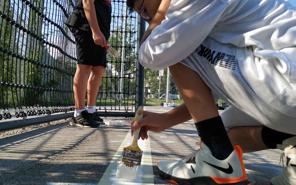 Die Linien im Fußball- und Basketballkäfig werden von den Jugendlichen neu gemalt