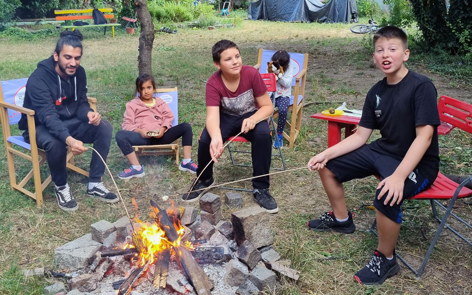 Eine Gruppe von Kindern sitzt um ein Lagerfeuer im Balugarten